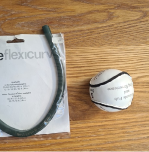 A photo of a Flexicurve ruler and a hurling ball on a wooden table top.