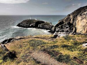 A photograph of a promontory with sea around it. On the promontory is a white lighthouse and building. This is South Stack, Anglesey/Ynys Môn, Wales